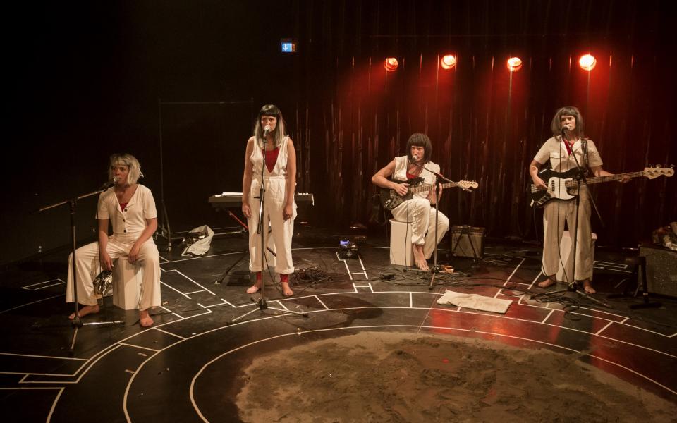 vier Personen stehen mit Musikinstrumenten auf einer Bühne. 